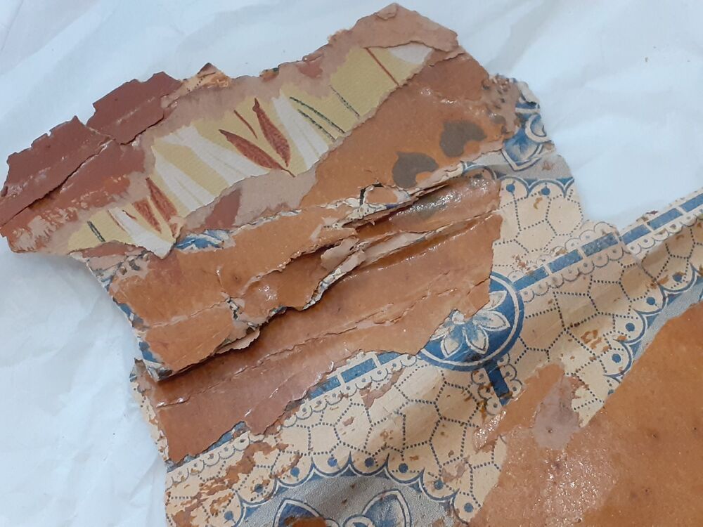 A close-up view of a surface showing layers scraped or peeled back to reveal different wallpaper designs and patterns.