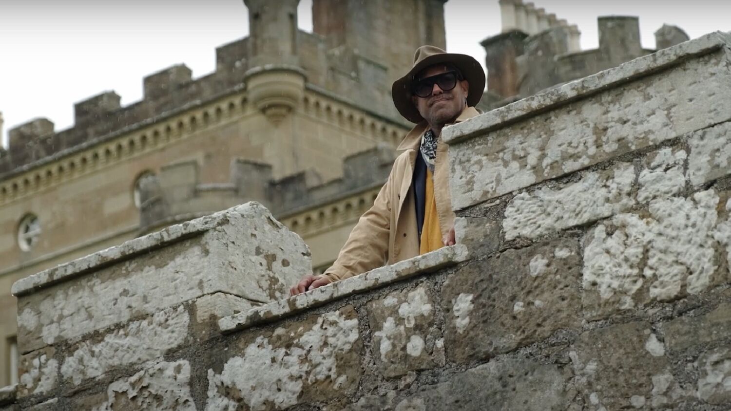 A man in a hat and sunglasses stands on the stone parapet of Culzean Castle, looking out across the grounds.
