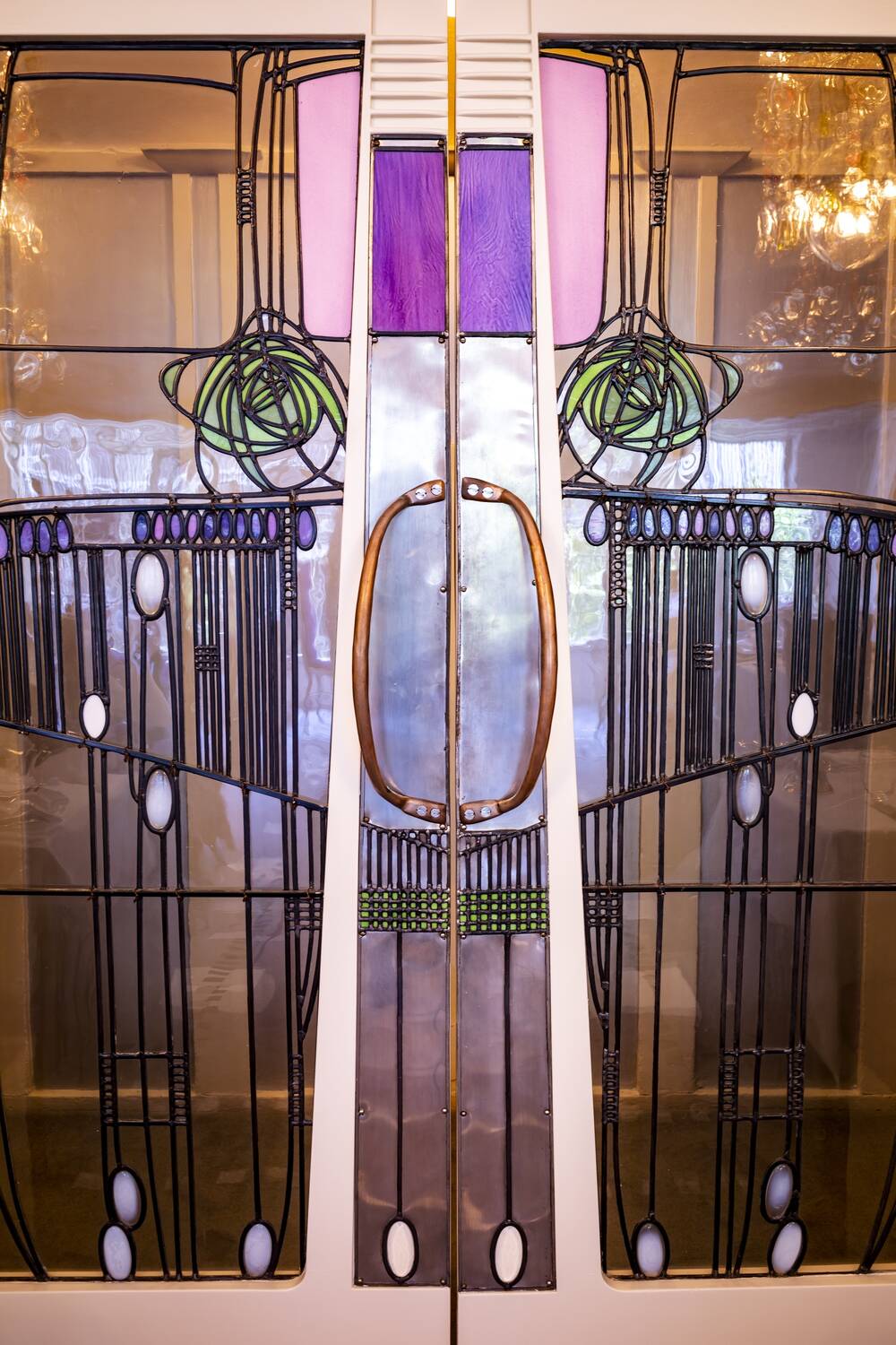 A detail of elaborate Mackintosh-designed entrance doors to a tea room. They are made of polished metal panels with green stylised roses on each side.