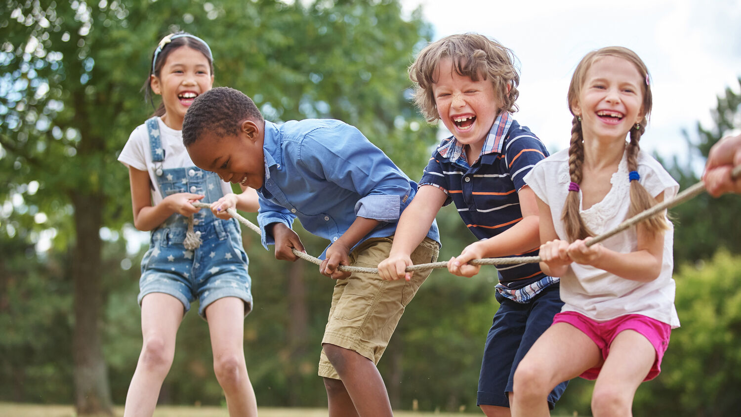 Four laughing children are pulling on a rope in a game of tug of war. All are wearing shorts and t-shirts.