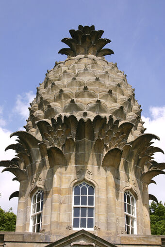 A close-up view of a stone folly in the shape of a pineapple. It has small windows at the base.