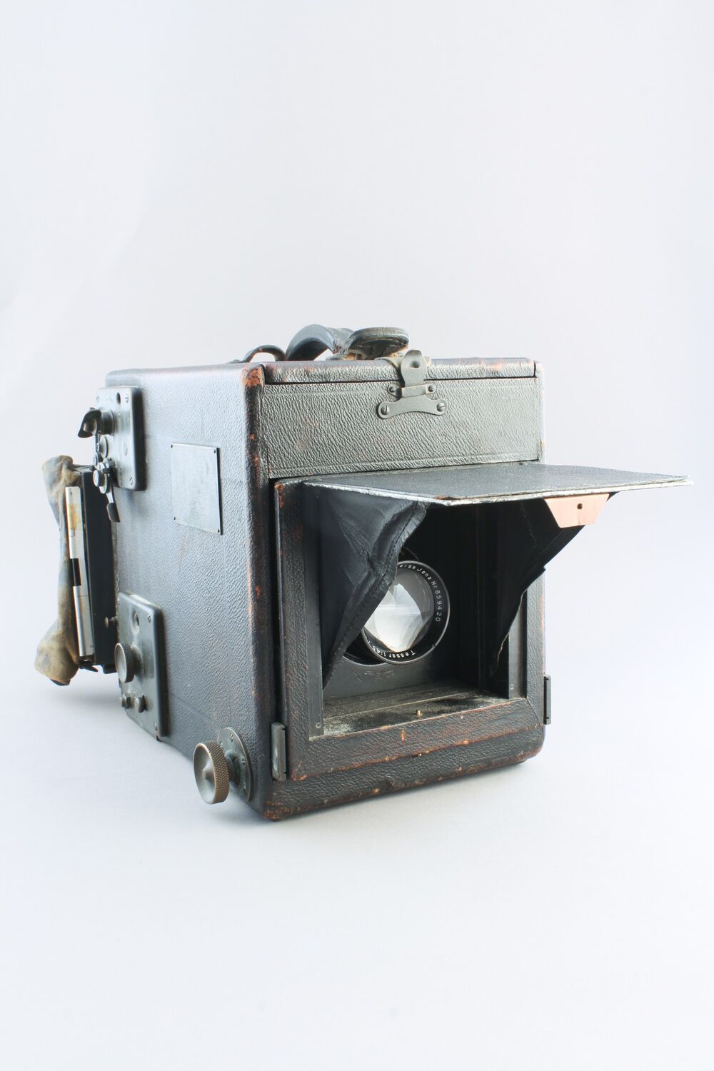 A black, box-shaped camera made from leather and metal, with a flap folded up to reveal the lens.