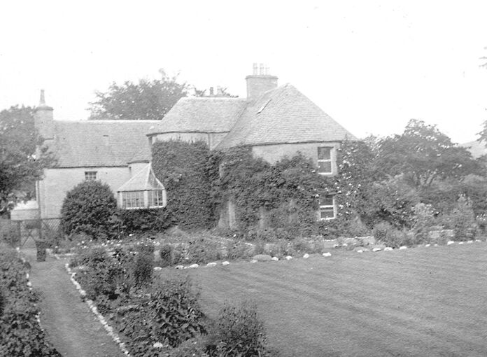 Black and white photograph of a large house with a large garden in front of it, with a well-mown lawn.