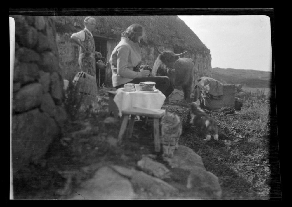 Black and white photo of people taking tea outside next to a Hebridean stone cottage