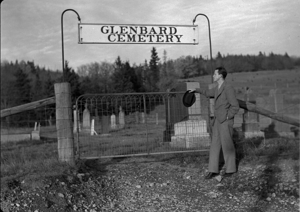 Black and white photograph of a man standing at the entrance to Glenbard Cemetery.