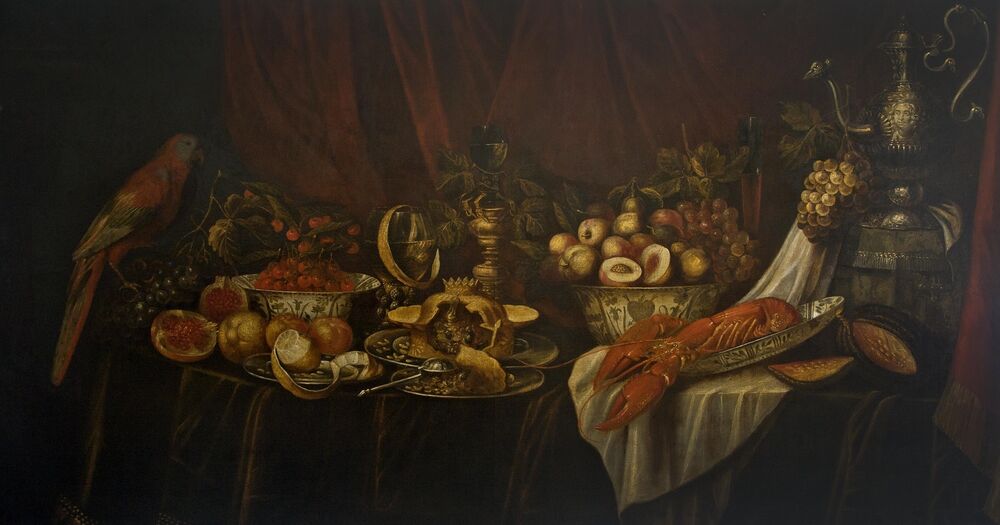 A long oblong-shaped oil painting of a still life of a richly laden dining table. Bowls are piled high with fruit; an elaborately constructed pie lies at the centre of the table; and a lobster is displayed to the right. A parrot sits on the left of the table. A jug shaped like a peacock stands on the right.