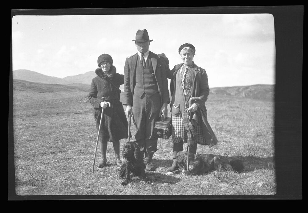 Black and white photograph of two woman and a man, with a black dog in front of them.