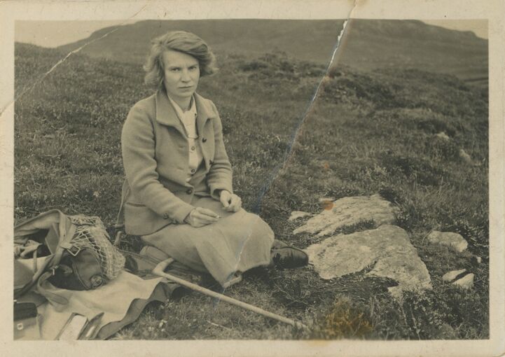 Black and white photograph of a woman sitting on the grass in the countryside.