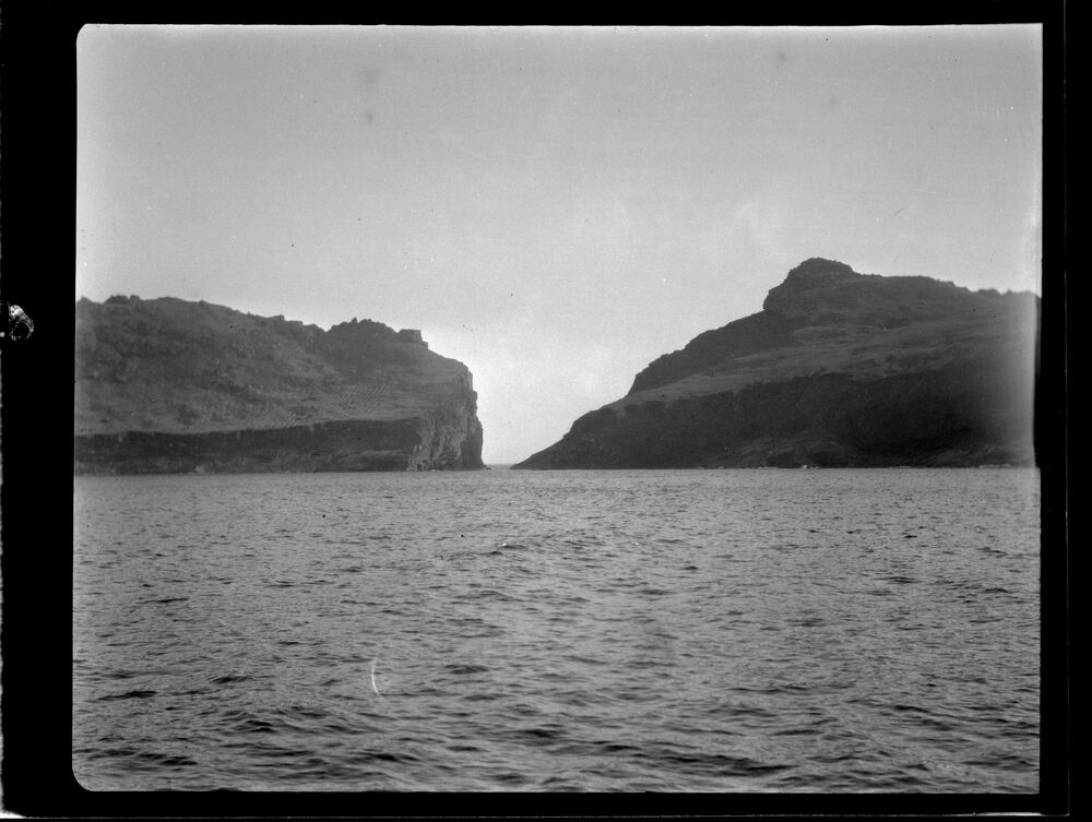 Black and white photograph taken from a boat, looking across the sea to two islands.