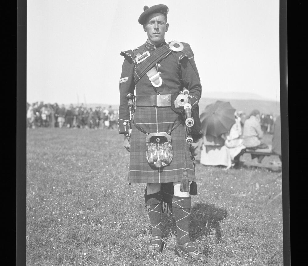 Black and white photograph of a man in a kilt, with a crowd of people behind at a Highland Games.