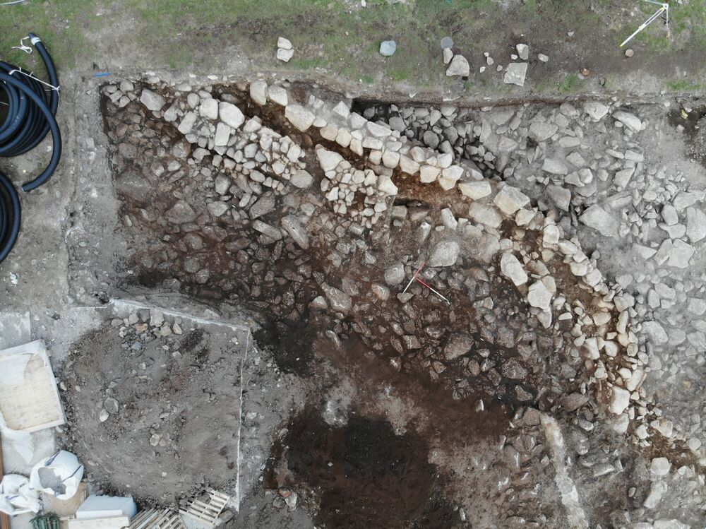 Overhead view of an archaeological excavation, showing lots of stones in a trench.