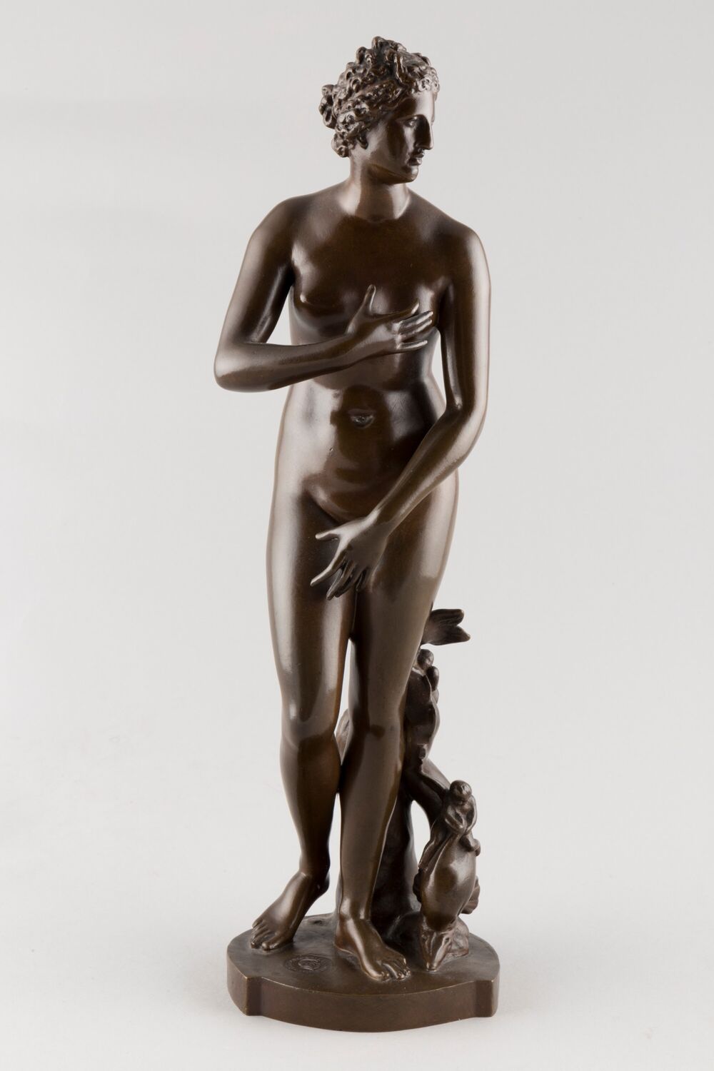 Bronze statue of Venus, looking to the side and with one hand covering her left breast and the other resting on her right thigh.