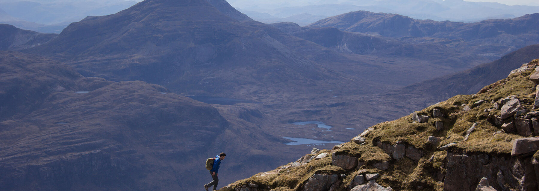 A young man hiking a knife-edged mountain ridge on the Liathach Ridge