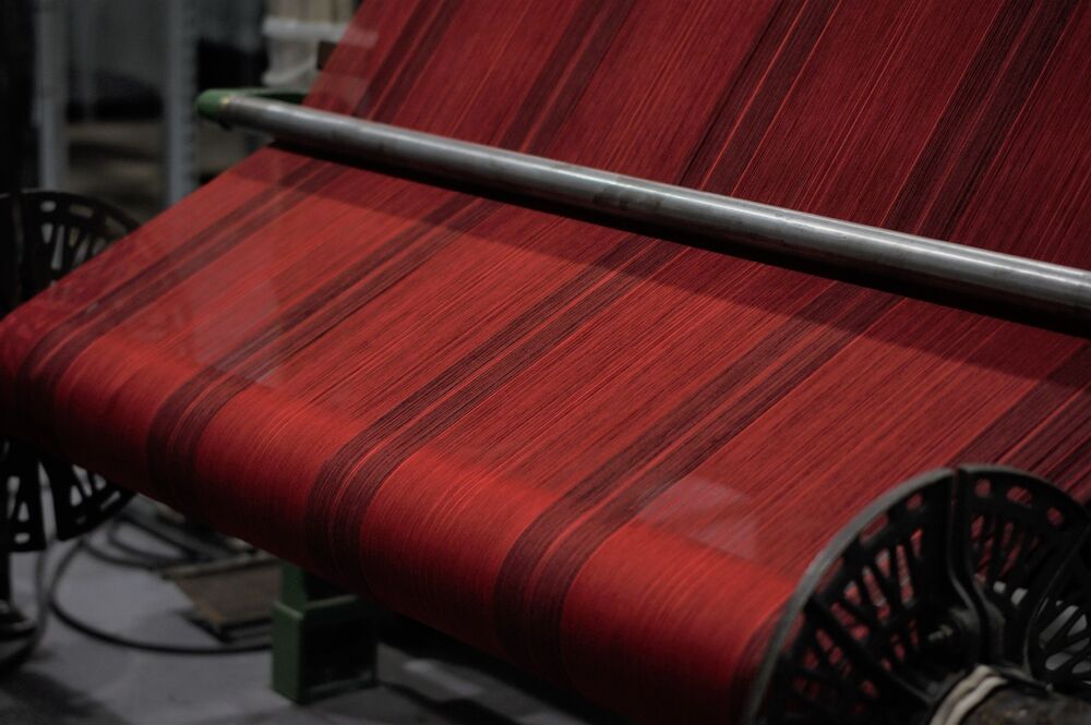 A red tartan being woven on a traditional loom.