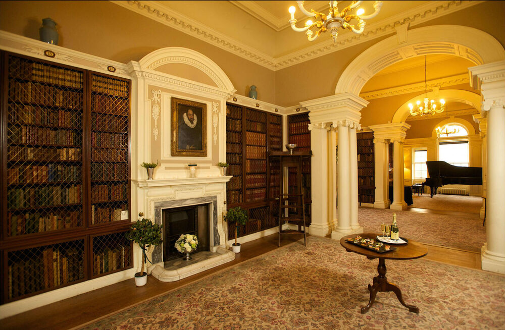 A grand library, with two archways leading to a room with a grand piano.