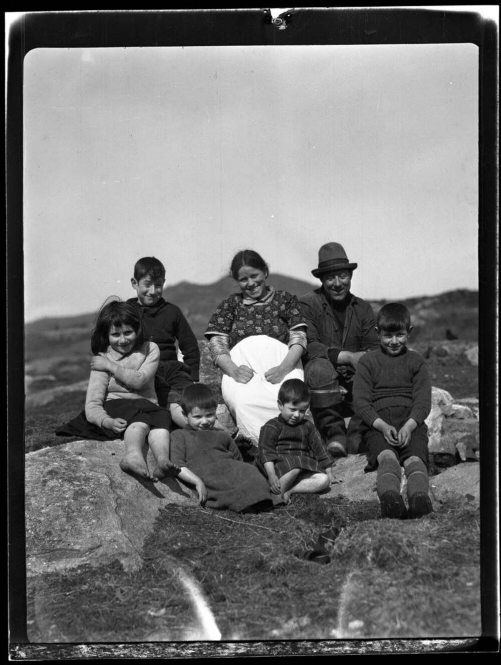 A black and white photo of a family seated on a hillside. Peigi Nill is at the centre, surrounded by children.