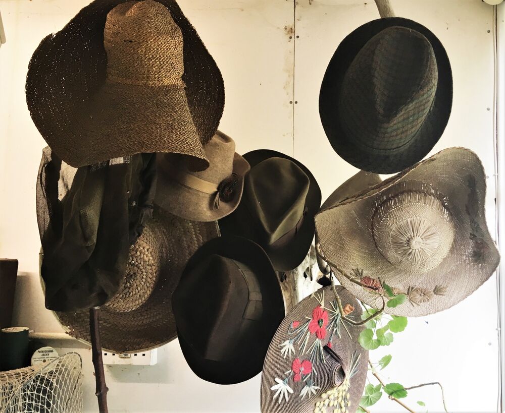 A group of hats are displayed on a hatstand. Most are brown felt but a couple are decorated with flowers and leaves.
