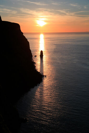 Cliffs silhouetted by the sunsetting over the sea.