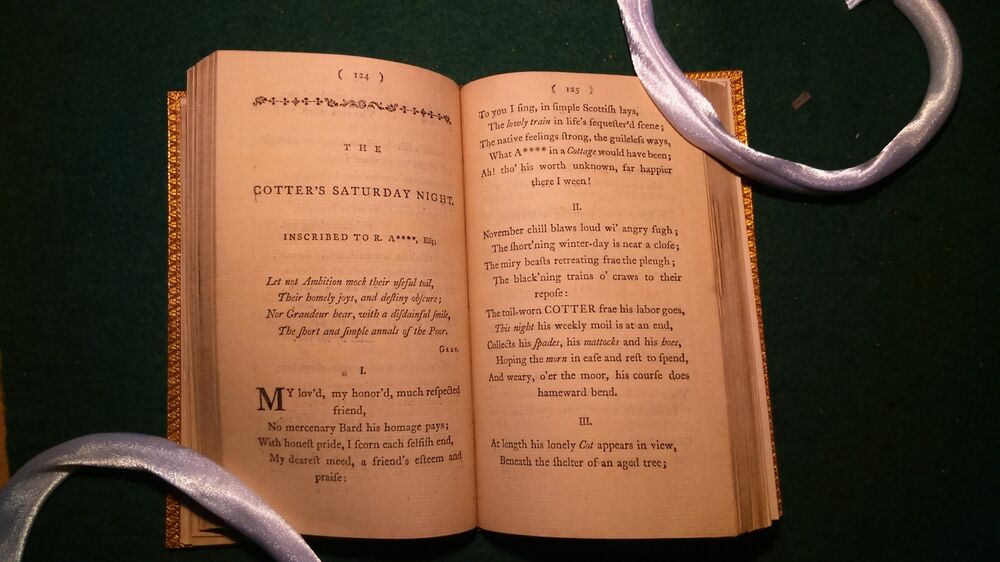 An old poetry book is displayed open against a black background. It is held open by two silk cords. The book is open at Robert Burns's poem The Cotter's Saturday Night.