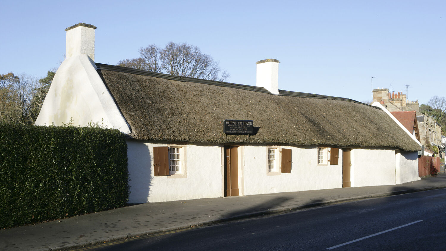 A white thatched cottage stands on the side of a road with a blue sky background.