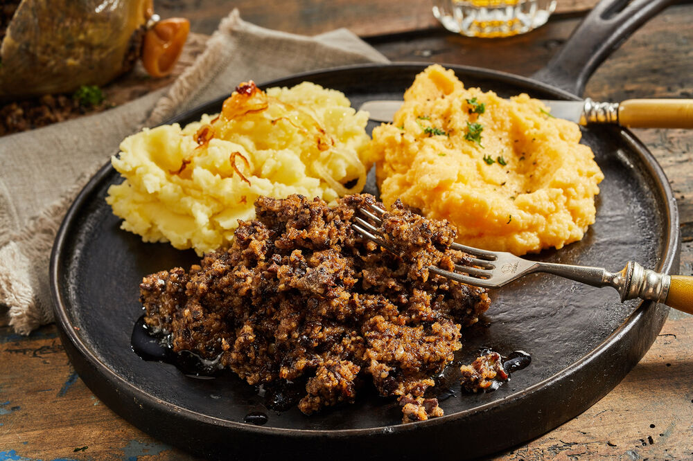 Rustic serving of haggis, neeps and tatties on a metal skillet showing the texture of the cooked meat with mashed turnip or swede and potato