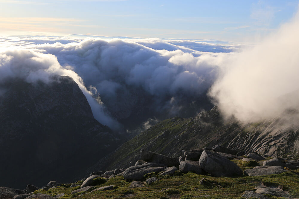 Cloud swirls around the top of a rocky, tall summit.