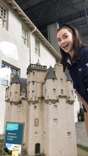 An augmented image of a castle appears on the gravel path in front of the Hill House. A lady stands beside it, smiling.