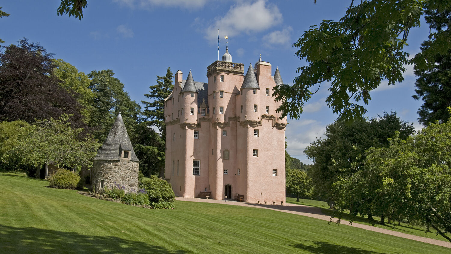 Craigievar Castle, a pink castle with turrets surrounded by a grassy lawn, with trees in the background.