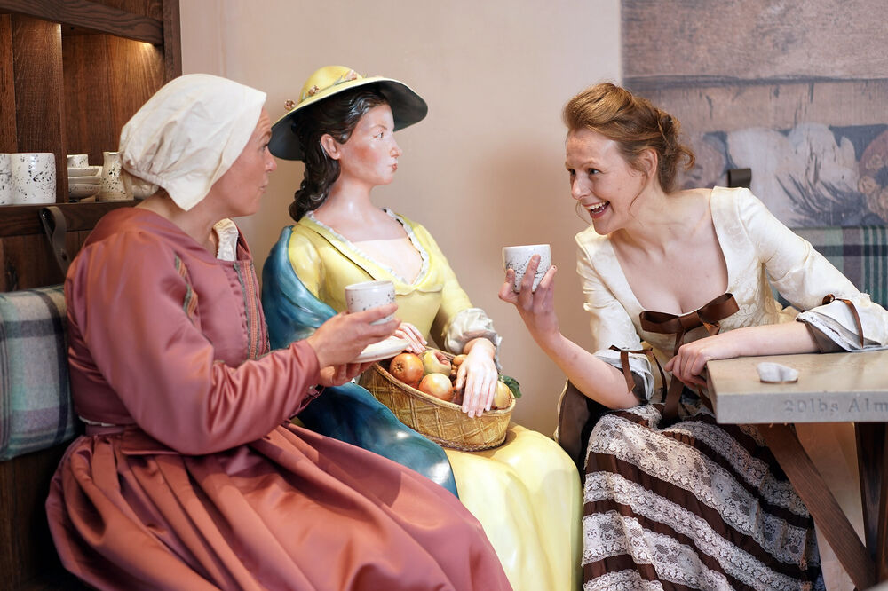 Two women in period costume enjoy coffee and a chat in a a coffee shop