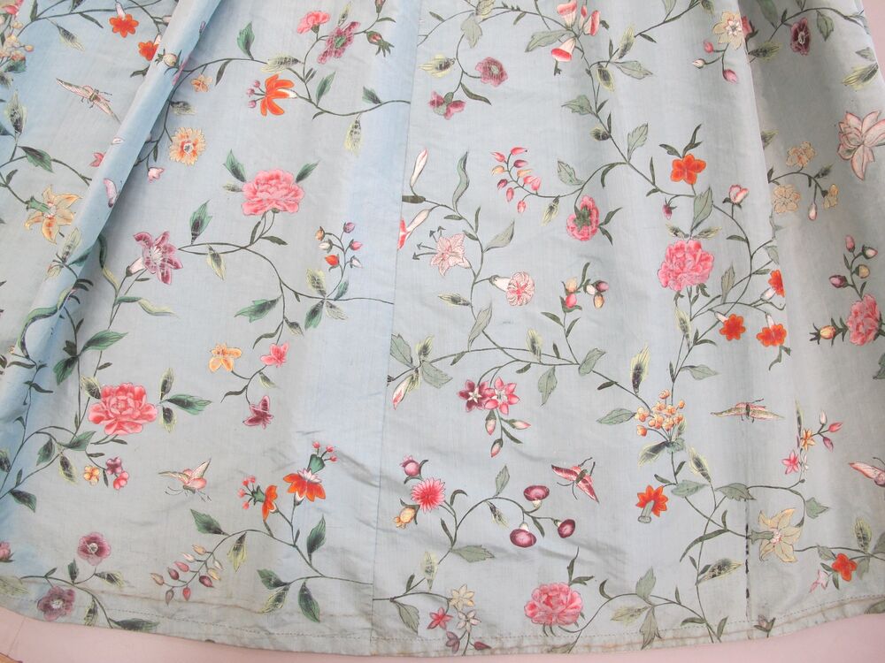 A close-up detail of a section of a blue silk fabric, with a flower pattern. The bottom hem line is clearly seen.