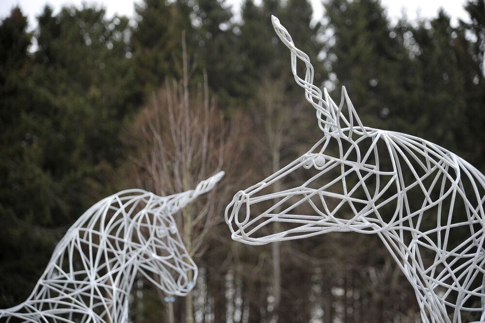 Two white woven unicorn statues stand outside, with woodland in the background.