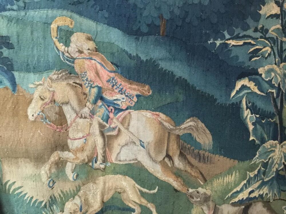 Detail from a tapestry showing a man riding a horse, blowing on a horn.