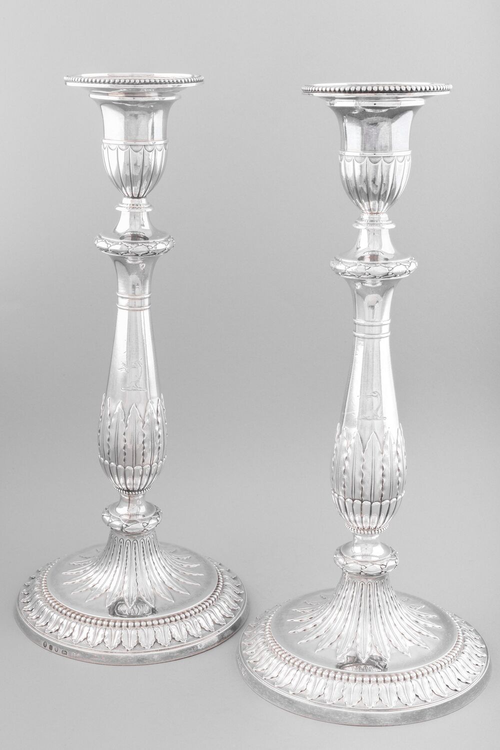 A pair of ornately carved silver candlesticks are displayed against a plain grey background.