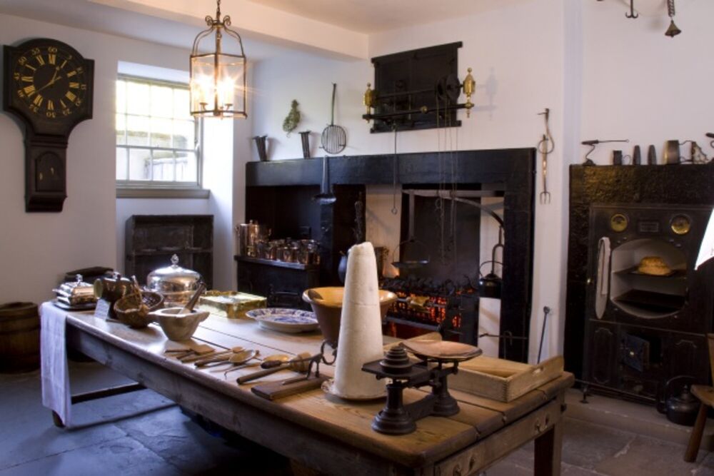 A Georgian kitchen, with lots of kitchen implements on the table in the centre of the room. There is a large range behind.
