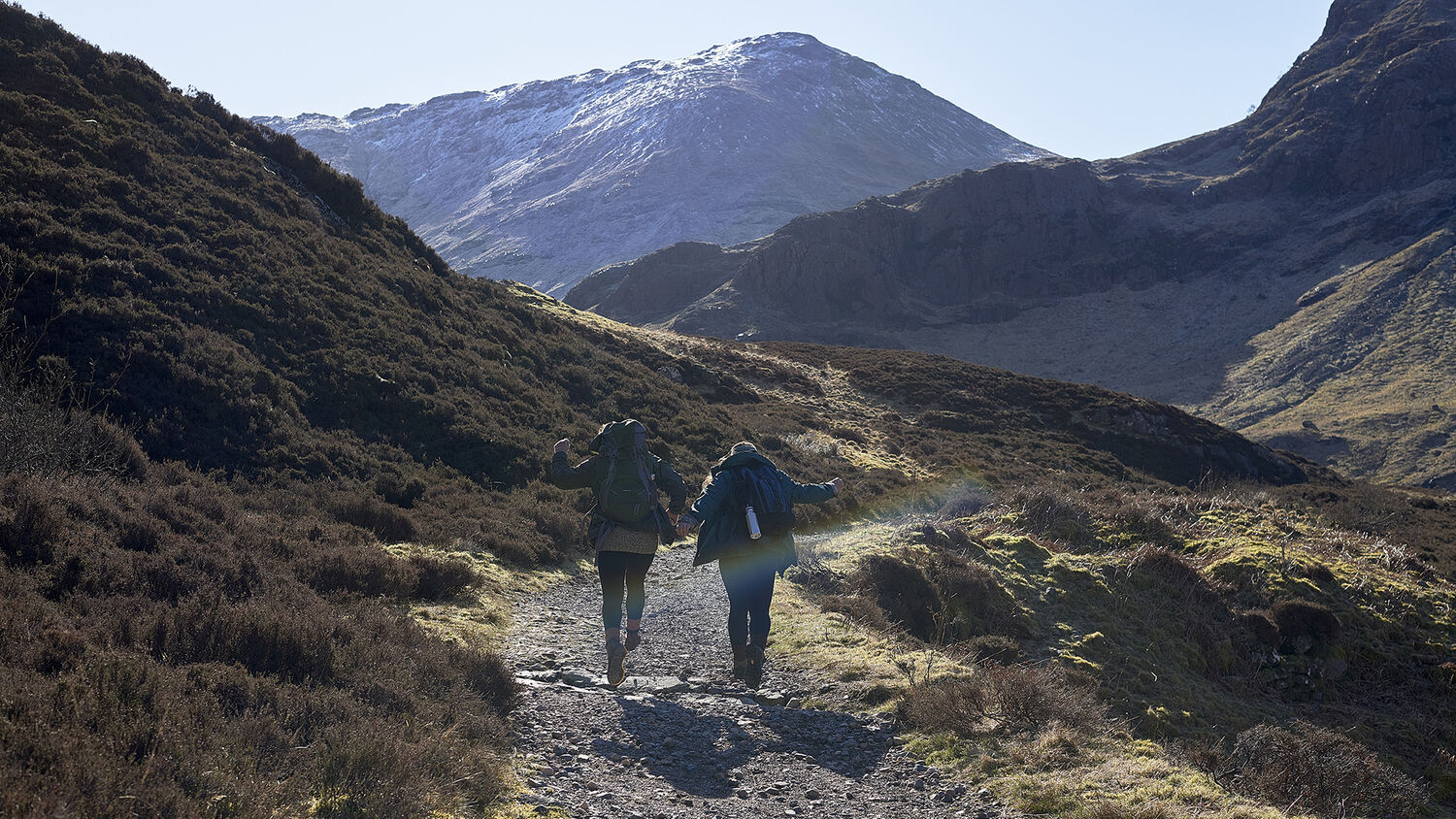 Two people walk on a path through the mountainous landscape of Glencoe.