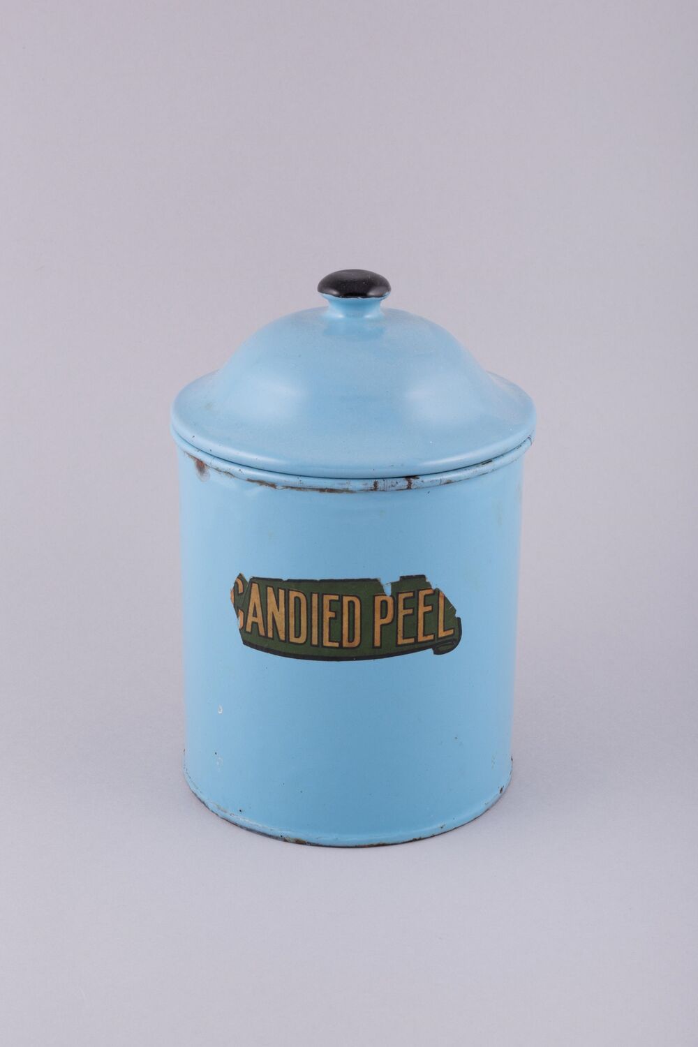 A blue metal cannister tin is displayed against a plain grey background. It has a slightly damaged label, from which can still be read Candied Peel.