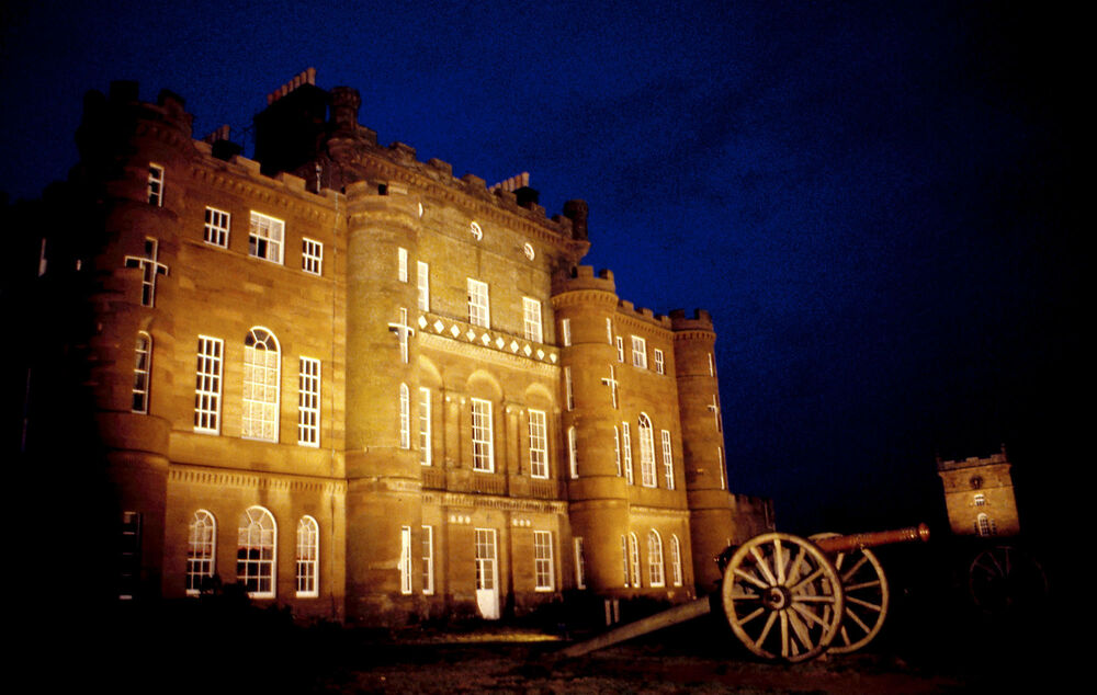 Culzean Castle lit by ground lights at night, with the cannon lit as well.