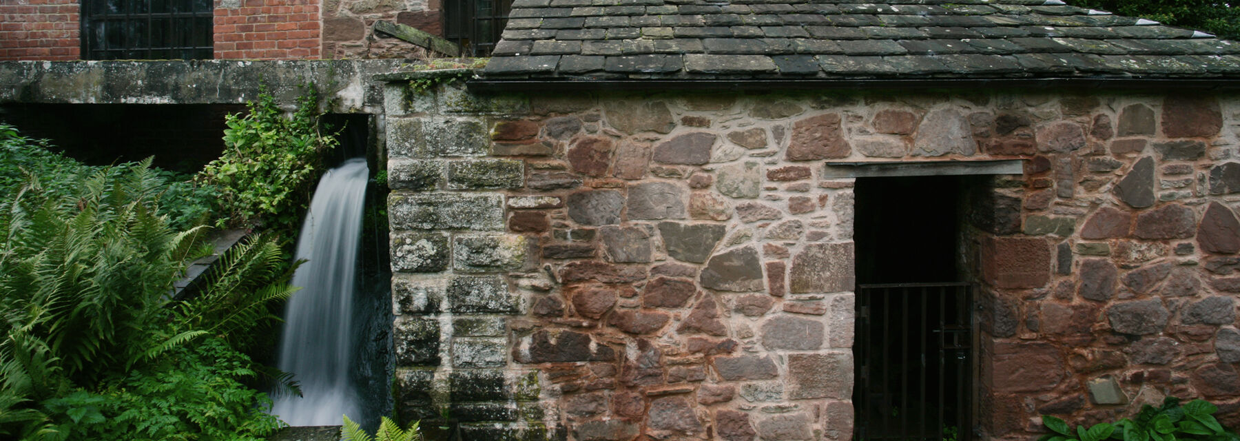 The exterior of the stone Barry Mill with the millrace outflow pouring out at the side.