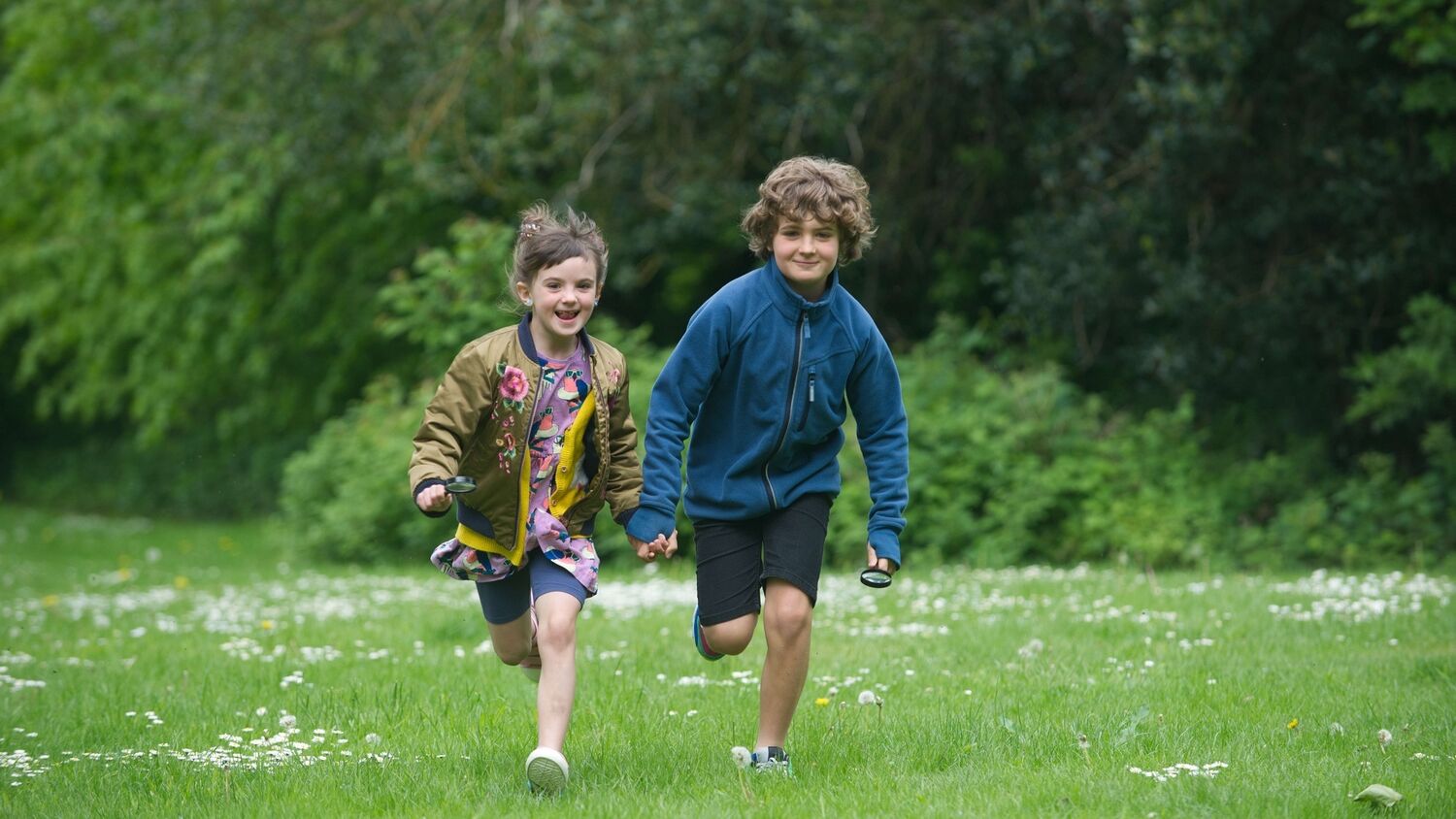 Two young boys run across a lawn towards the camera.