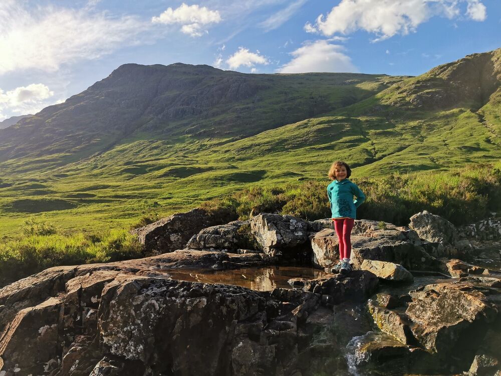 Small girl stands by a rock in a mountain landscape