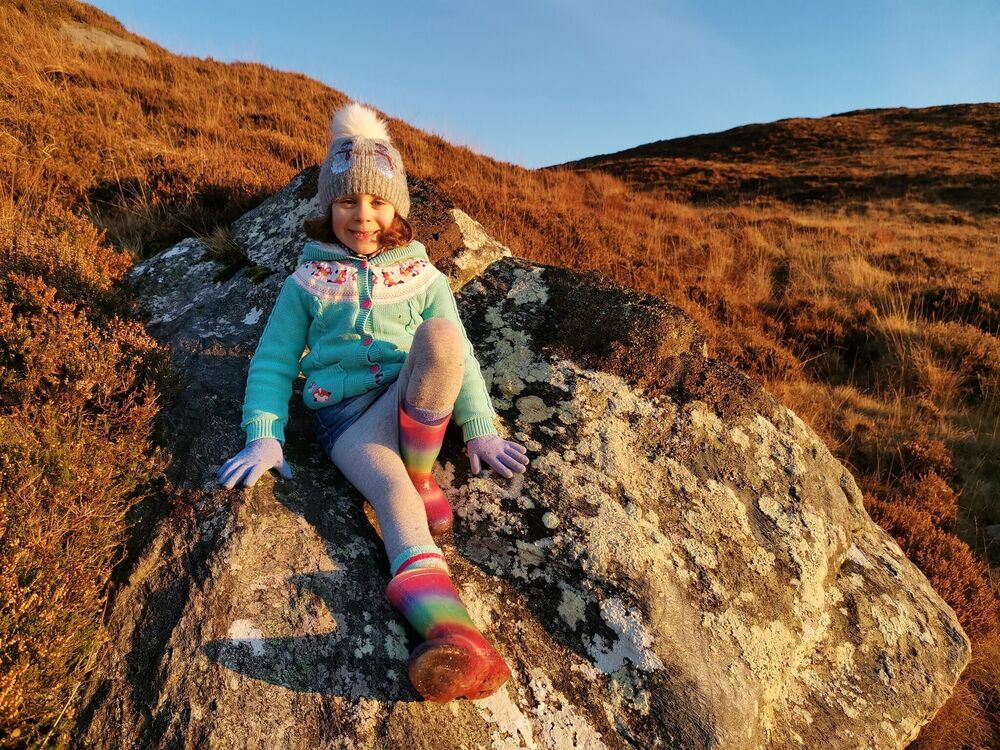 A small girl sits on rocks, in a rugged landscape