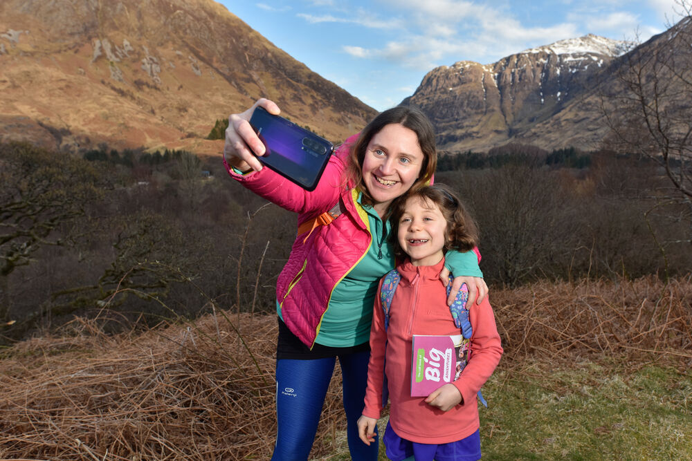 A woman and young girl pose for a selfie with mountains behind