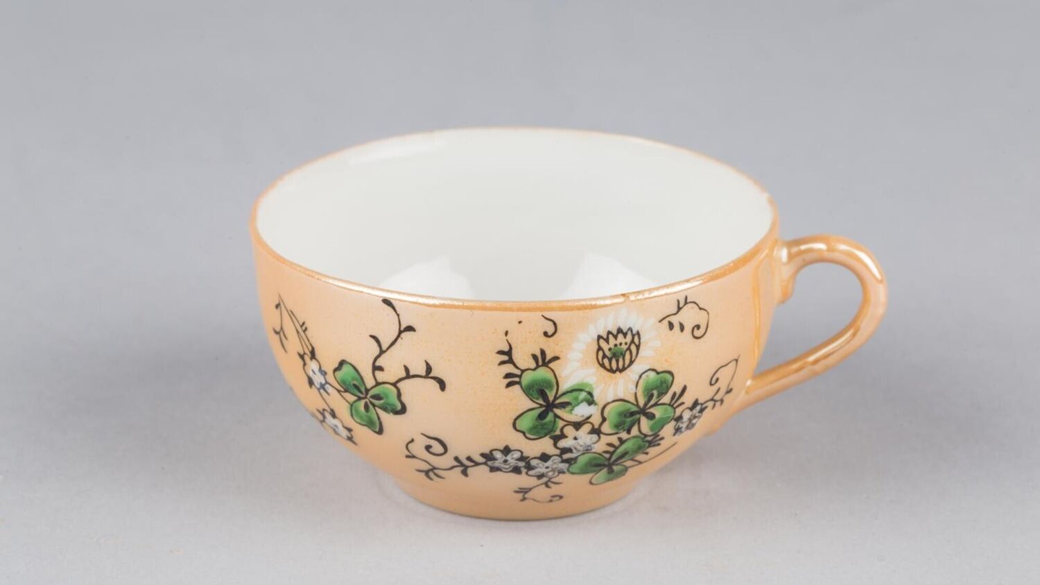 An intricately patterned child's teacup in a peach colour with a clover pattern.