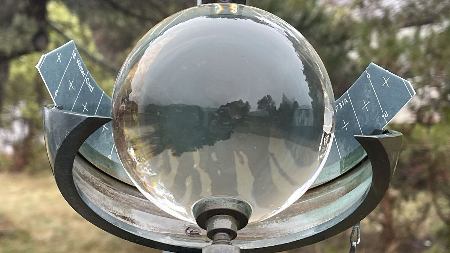 A close-up view of a sunlight recorder, which consists of a glass ball (rather like a crystal ball) mounted on a sundial-type frame. A metal structure half encircles it, with markings on it to chart the sun's progress.