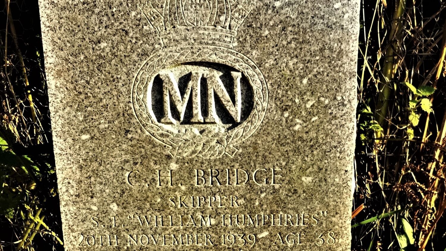 A close-up of a gravestone. At the top is a coat of arms with the letters MN carved inside. Beneath the engraving reads: C H Bridge, Skipper, S. T. ‘William Humphries’, 20th November 1939, Age 38.