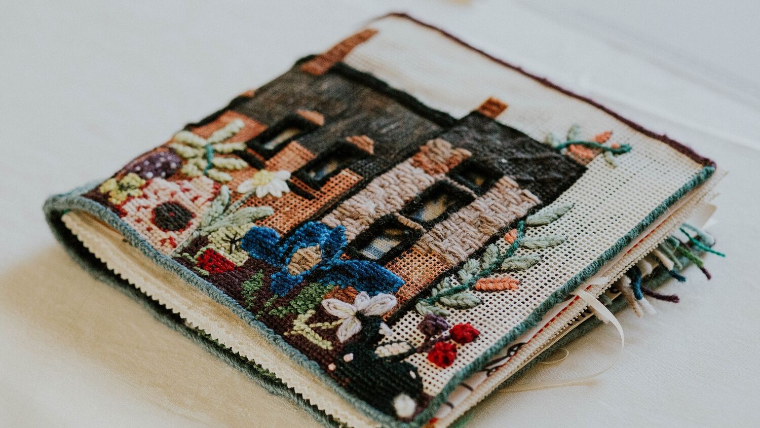 A fabric book is displayed against a plain grey background. The front cover is a tapestry of a castle with colourful flowers in the foreground.