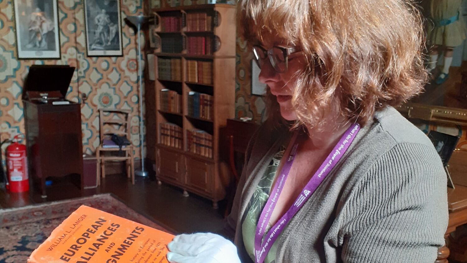 A close-up of a woman with white conservation gloves holding a hardback book with an orange cover.