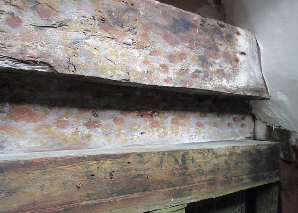 A close-up photo of two ancient wooden ceiling beams, featuring faint painted decoration in shades of brown and orange.
