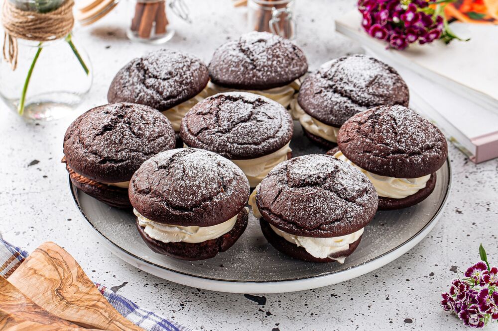 A plate of chocolate whoopie pies, with a buttercream filling. They have been sprinkled with icing sugar.