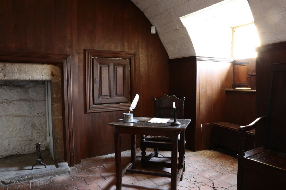 The strong room at Culross Palace, with wood-panelled walls either side of a stone fireplace. A chair and desk stand in the corner of the room, with a quill and candlestick upon it.